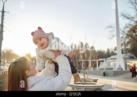 Glückliche harmonische Familie im Freien. Mutter wirft Baby, lachend und spielend im Sommer Stockfoto