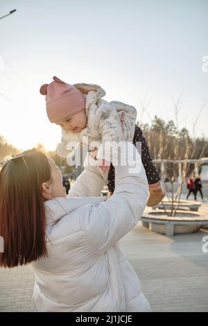 Glückliche harmonische Familie im Freien. Mutter wirft Baby, lachend und spielend im Sommer Stockfoto