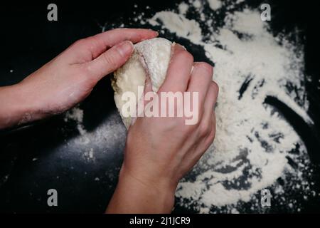 Pizzateig auf einem schwarzen Tisch mit Händen Stockfoto