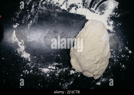 Pizzateig auf einem schwarzen Tisch mit Händen Stockfoto