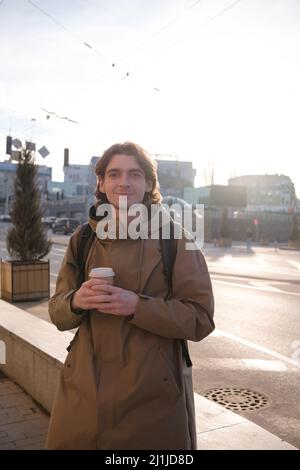 Glücklicher lächelnder Geschäftsmann, der mit einer Kaffeetasse und einem modernen Smartphone im Freien zur Arbeit geht, erfolgreicher Arbeitgeber, der in der Pause Mobiltelefon verwendet Stockfoto