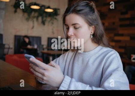 Glücklich lächelnd wunderschöne Frau in modischen Brillen lesen angenehme Textnachricht auf dem Handy, während im Café während der Freizeit sitzen. Stockfoto