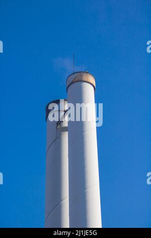 Kamine eines Holzpellet-Kraftwerks für die lokale Wärmeversorgung vor blauem Himmel Stockfoto