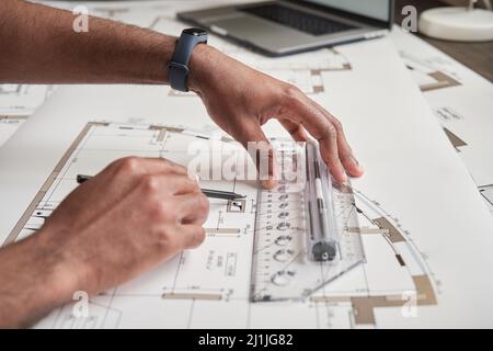 Nahaufnahme eines nicht erkennbaren Mannes mit einer Fitnessuhr, der beim Erstellen des Baudokuments ein Lineal verwendet Stockfoto