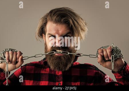 Brutaler bärtiger Mann beißt Stahlkette mit starken Zähnen, Bisskorrektur Stockfoto