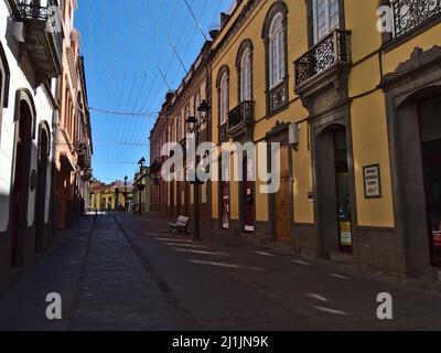 Blick auf die leere Straße in der historischen Innenstadt von Arucas auf der nördlichen Gran Canaria, Spanien mit Geschäften in alten Gebäuden an sonnigen Tagen. Stockfoto