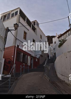 Schöner Blick auf eine schmale Gasse in der Altstadt von Puerto de Mogan, Gran Canaria, Spanien am Abend mit Wäscherei und bewölktem Himmel. Stockfoto