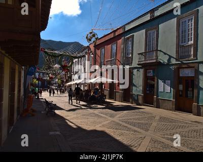 Touristen genießen die Nachmittagssonne in der Fußgängerzone der Kleinstadt Teror, Gran Canaria, Spanien mit historischen Gebäuden und Weihnachtsschmuck. Stockfoto