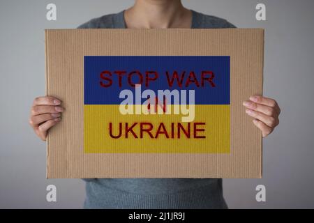 Eine Frau hält das Papierschild „STOP WAR IN UKRAINE“ auf dem Hintergrund der ukrainischen Flagge Stockfoto