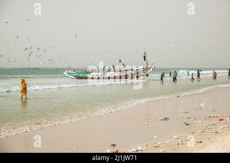 Fischer, die mit ihren farbenfrohen Booten mit frisch gefangenem Fisch, Nouakchott, Mauretanien, auf den Fischmarkt kommen Stockfoto