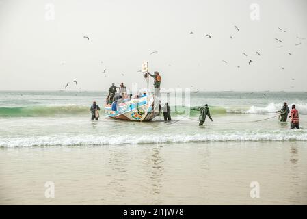 Fischer, die mit ihren farbenfrohen Booten mit frisch gefangenem Fisch, Nouakchott, Mauretanien, auf den Fischmarkt kommen Stockfoto