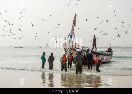 Fischer, die mit ihren farbenfrohen Booten mit frisch gefangenem Fisch, Nouakchott, Mauretanien, auf den Fischmarkt kommen Stockfoto