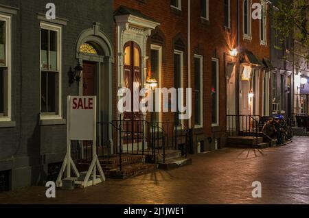 Ein Foto von beleuchteten Häusern in der Nacht mit einem zum Verkauf Schild vor einem Haus Stockfoto