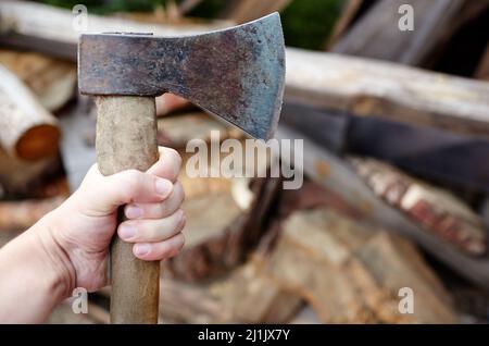 Mann mit Axt. Axt in der Hand. Ein starker Mann hält eine Axt in den Händen vor dem Hintergrund von Feuerholz. Selektiver Fokus, unscharfer Hintergrund Stockfoto