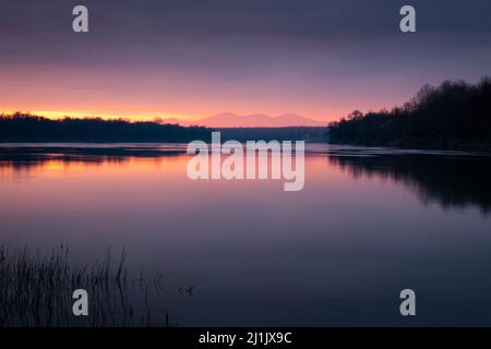 Dramatischer Sonnenuntergang über dem Fluss Sava mit einem Berg in trüber Glut - wunderschöne Naturlandschaft Stockfoto
