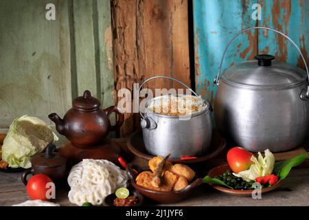 Nasi Liwet Sunda lengkap, würzig gedämpfter Reis, indonesischer Stil mit gebratenen Sardellen, Chili, ZitronenBasilikum Kemangi auf Kastrol, traditionelle Pfanne Stockfoto