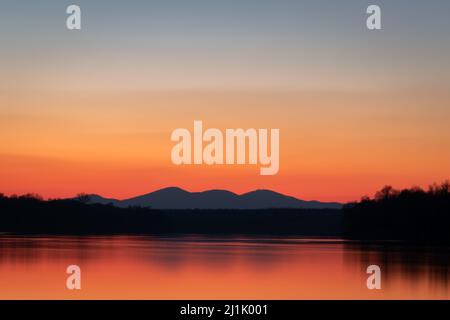 Landschaft des Flusses Sava, Wald und ferne Bergsilhouetten, klarer Himmel mit leuchtendem Rot und Orange am Horizont während der Dämmerung Stockfoto