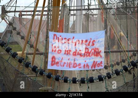 Greetsiel, Deutschland. 26. März 2022. Ein Banner mit der Aufschrift „Dieselpreis. Wo ist die Richtlinie? Unternehmen in Not hängen an einem Angelschneider im Hafen. Aufgrund der enormen Preiserhöhung von Schiffsdiesel lohnen sich Fischereifahrten auf der Nord- und Ostsee derzeit nicht für Fischer. Die Kutter bleiben oft in den Häfen. Quelle: Lars Klemmer/dpa/Alamy Live News Stockfoto