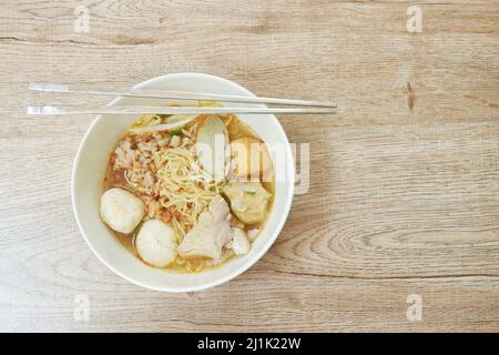 Eiergelbe Nudeln Nudeln Nudeln Belag in Scheiben gekochtes Schweinefleisch und Ball in würzige tom Yum Suppe auf Schüssel Stockfoto