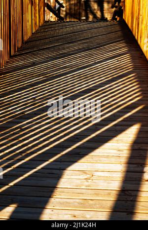 Schatten auf Holzsteg mit Holzgeländer bilden vertikale diagonale Boxen Stockfoto