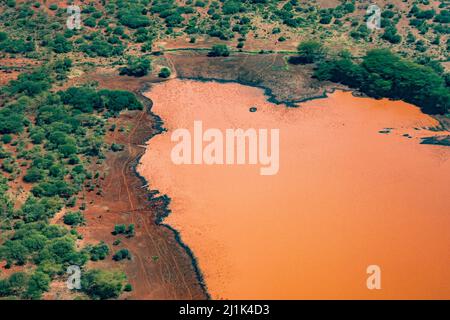 Wunderschöne Luftaufnahme des schlammigen Ufers und des orangefarbenen Wassers eines Wasserlochs in der Savanne Kenias Stockfoto