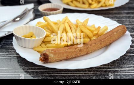 Deutsche Bratwurst oder gegrillte Wurst mit Pommes frites, Senf und Ketchup auf einem Teller in einem Straßenrestaurant, ungesundes Fast Food, ausgewählter Fokus, nar Stockfoto