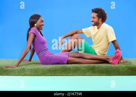 Genießen Sie die eine und andere Gesellschaft. Ein junges afrikanisches Paar, das zusammen auf dem Gras sitzt. Stockfoto