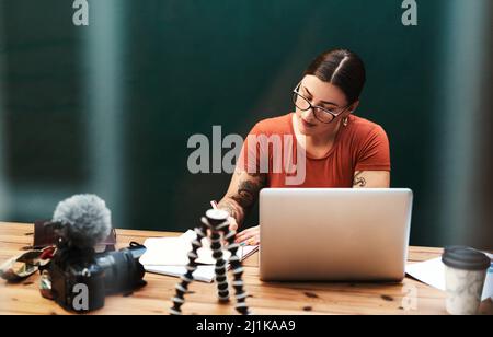 Das Aufschreiben hilft mir, mich daran zu erinnern. Eine kleine Aufnahme einer attraktiven jungen Geschäftsfrau, die allein an ihrem Schreibtisch sitzt und in ihr Notizbuch schreibt. Stockfoto