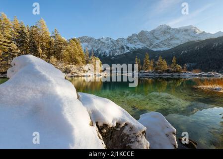 Schneebedeckte Bergwälder und das Wettersteingebirge mit Zugspitze in der Nachmittagssonne spiegeln sich im türkisfarbenen Wasser des Eibsees in Bayern Stockfoto