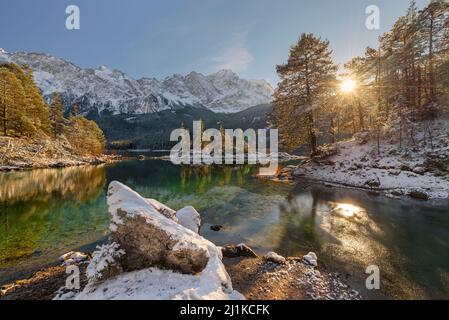 Schneebedeckte Bergwälder und das Wettersteingebirge mit Zugspitze in der Nachmittagssonne spiegeln sich im türkisfarbenen Wasser des Eibsees in Bayern Stockfoto