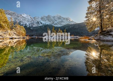 Schneebedeckte Bergwälder und das Wettersteingebirge mit Zugspitze in der Nachmittagssonne spiegeln sich im türkisfarbenen Wasser des Eibsees in Bayern Stockfoto