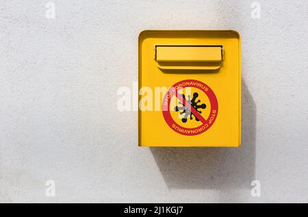 Gelber Briefkasten an der Wand mit Stop Corona Virus Zeichen Stockfoto