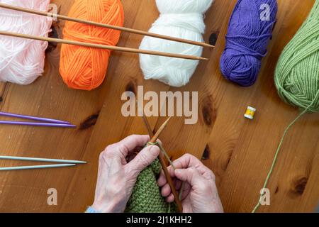 Hände älterer Menschen mit Arthritis genießen das Stricken in einem flachen Lay-Stil, umgeben von Strickzubehör Stockfoto