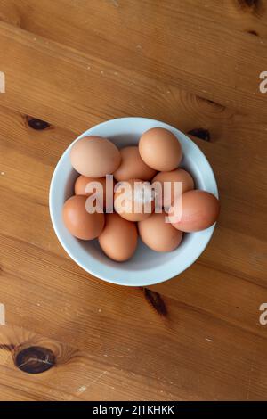 Eine flache Lay-Stil Bild einer Schüssel mit Eiern auf einem Holzstil Hintergrund mit einer Feder auf dem oberen Ei Stockfoto