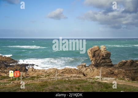 Felsen am Rand des Wassers vom Strand. Wolkiger Himmel im Sonnenlicht. Bekannter Surfspot in La Torche in der Bretagne in der Nähe von Plomeur. Stockfoto