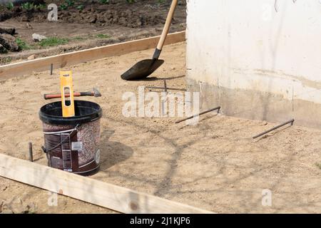 Vorbereitung des Blindbereichs des Fundaments. Grundlegende Schalungsmarkierung. Sackbereich Bau in der Nähe des Hauses. Hammer Eisenarmatur am Fuß des Hauses Stockfoto