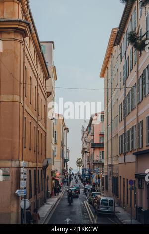 Nizza, Frankreich - 10. März 2022: Blick auf eine typische schmale Straße mit traditionellen pastellfarbenen Gebäuden in Nizza, einem berühmten Touristenziel Stockfoto