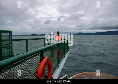 San Juan Island, WA USA - ca. November 2021: Blick auf eine ältere Frau in einer hellen, orangen Jacke, die vom Washingto aus auf den Pazifik blickt Stockfoto