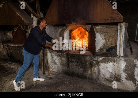 Ein Mann fügt brennendes Reisig in einen traditionellen Steinofen in der Dorfbäckerei von Akdeniz ein. Ein Teil des Brennholzes stammt von den wilden Pistaziensträuchern, die um das Dorf wachsen. Akdeniz (türkisch für "Mittelmeer") bietet einen Einblick in das typische Landleben Zyperns, Türkische Republik Nordzypern (TRNK). Stockfoto