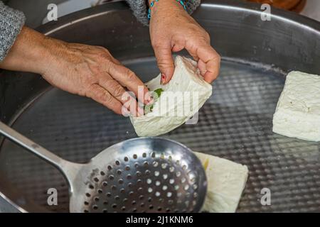 Im Dorf Akdeniz, was übersetzt Mittelmeer bedeutet, bekommt man einen Eindruck vom typischen zypriotischen Landleben. Jeden Tag die Käsefrau Fatma Haloumi (Hellim), die berühmteste zypriotische Spezialität aus Ziege- und Schafsmilch. Die gegarten und gesalzenen Hellim-Stücke werden mit frischer Minze gerieben. Zubereitung der Käsespezialität Hellim oder Halloumi in Akdemiz, Nordzypern Stockfoto