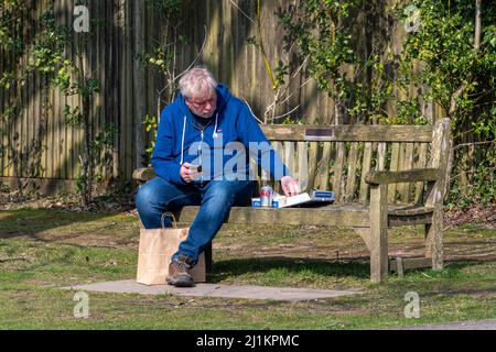 Mann, der Fisch und Chips zum Mitnehmen mit einer Dose Coca Cola auf einer Dorfbank, England, GB, isst Stockfoto