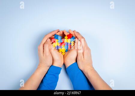Konzept des Welt-Autismus-Tages. Erwachsene und Kinder Hände halten Puzzle Herz auf hellblauem Hintergrund. Draufsicht Stockfoto