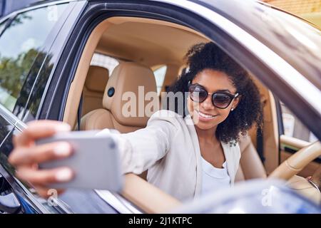 Selfies auf dem Fahrersitz fangen. Eine kurze Aufnahme einer attraktiven jungen Geschäftsfrau, die Selfies macht, während sie am Morgen zur Arbeit fährt. Stockfoto