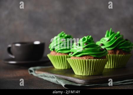 St. Patrick's Day Kaffee und hausgemachte Cupcakes mit grüner Schlagsahne und Schokoladenstreuseln auf braunem Hintergrund. Stockfoto