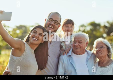 Im Leben geht es darum, diese glücklichen Momente zu sammeln. Aufnahme einer glücklichen Familie, die zusammen ein Selfie im Park macht. Stockfoto