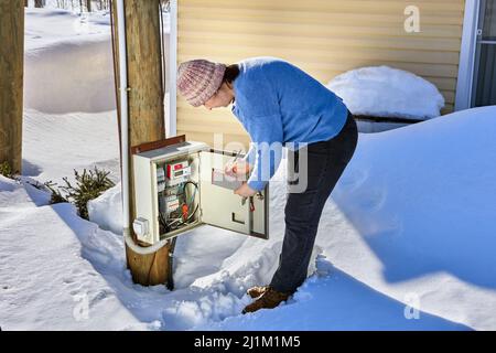 Eine Außenschalttafel mit einem elektrischen Messgerät, eine Frau, die Messwerte abnimmt. Stockfoto