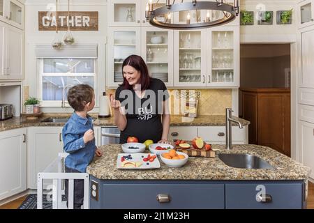 Die Schwangeren und ihr Kleinkind verbringen gemeinsam Zeit in der Küche und bereiten gesunde Snacks zu Stockfoto