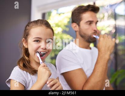 Dank DVDAD kann ich mir die Zähne selbst putzen. Eine kleine Aufnahme eines hübschen Vaters und seiner Tochter, die sich zu Hause im Badezimmer die Zähne putzten. Stockfoto