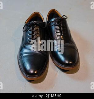 Schuhe mit schwarzen Kleidern und braunen Rändern auf grauem Zementboden. Alles gefesselt. Stockfoto