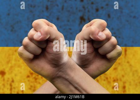 Konfrontation und Wettbewerb. Der Mann kreuzte seine Arme über seine Brust und hielt seine Fäuste vor der ukrainischen Flagge fest. Das Konzept von Stockfoto